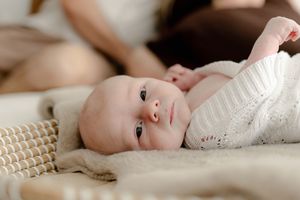 Sweet newborn baby lying on textured cream blanket looking up with bright eyes.