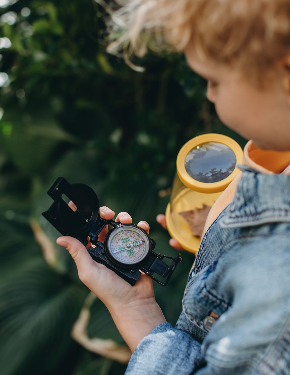 A person in denim holds a vintage camera while taking photos outdoors in natural lighting.