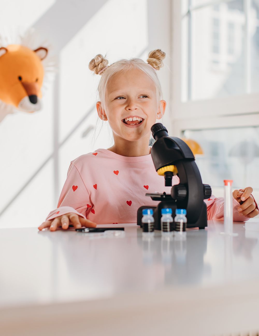 Young scientist examining samples through microscope in bright laboratory setting with orange accents.