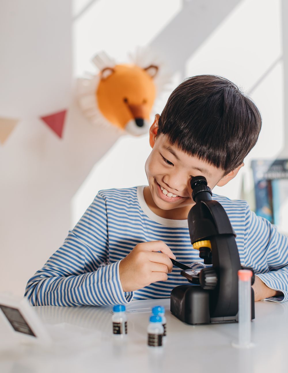 Child in striped shirt explores and learns while using a microscope in a bright indoor setting.