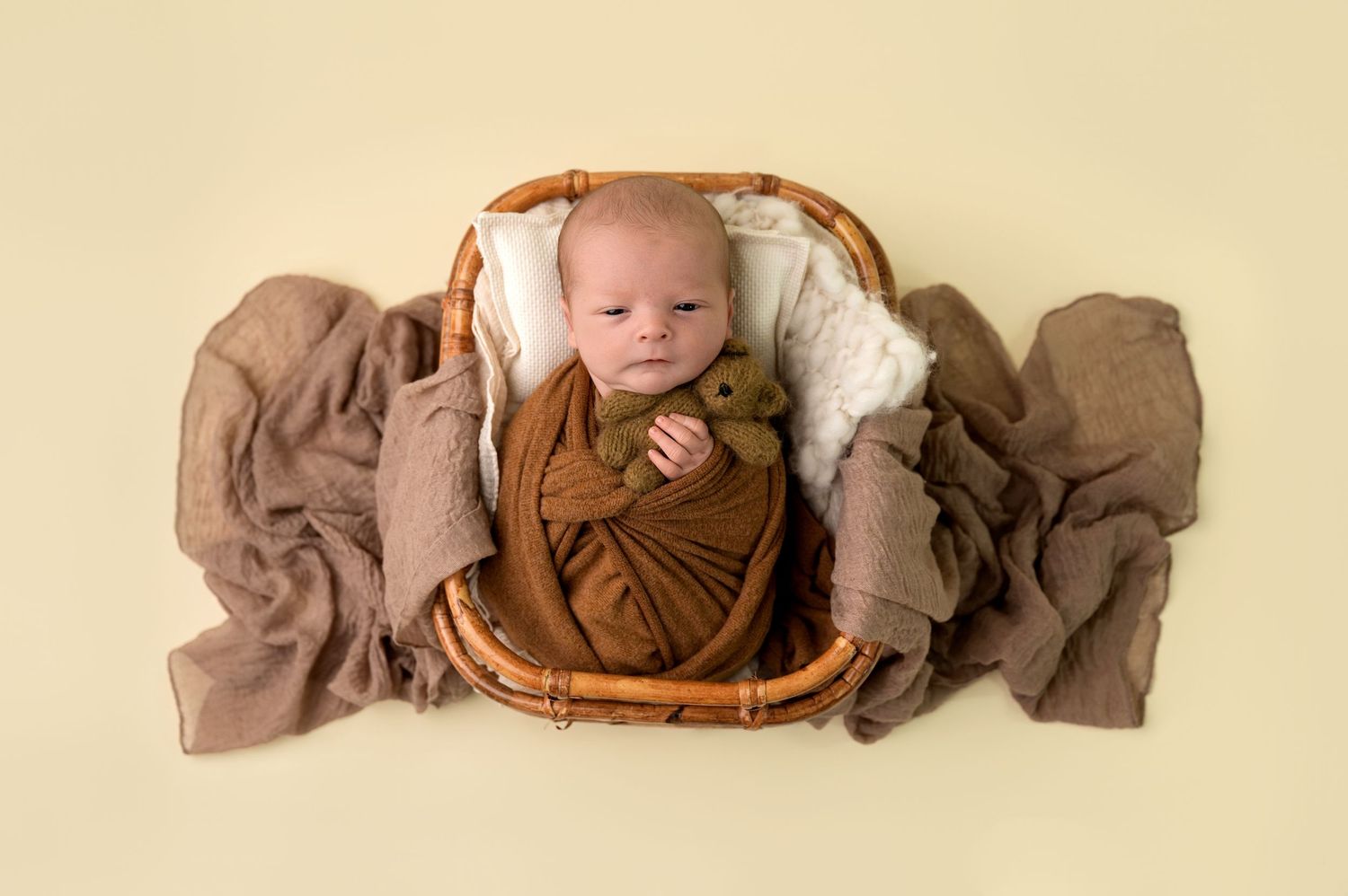 Panoramic series of baby lying in brown basket with fabric on beige background.