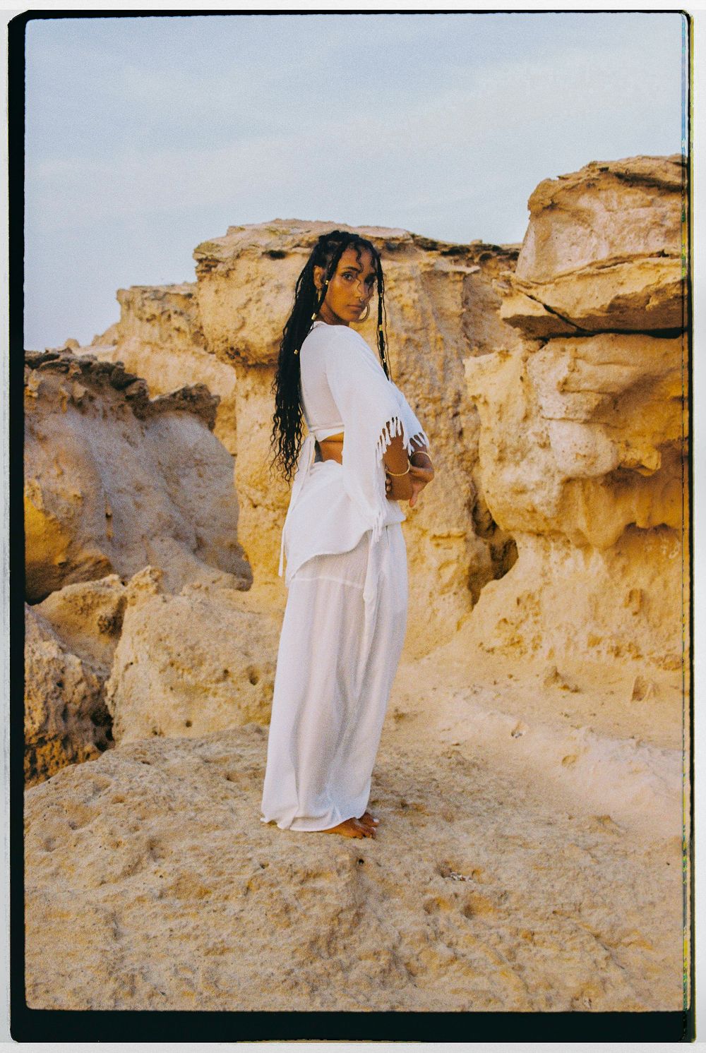 Figure in flowing white garments stands against desert rock formations in a series of ethereal poses.