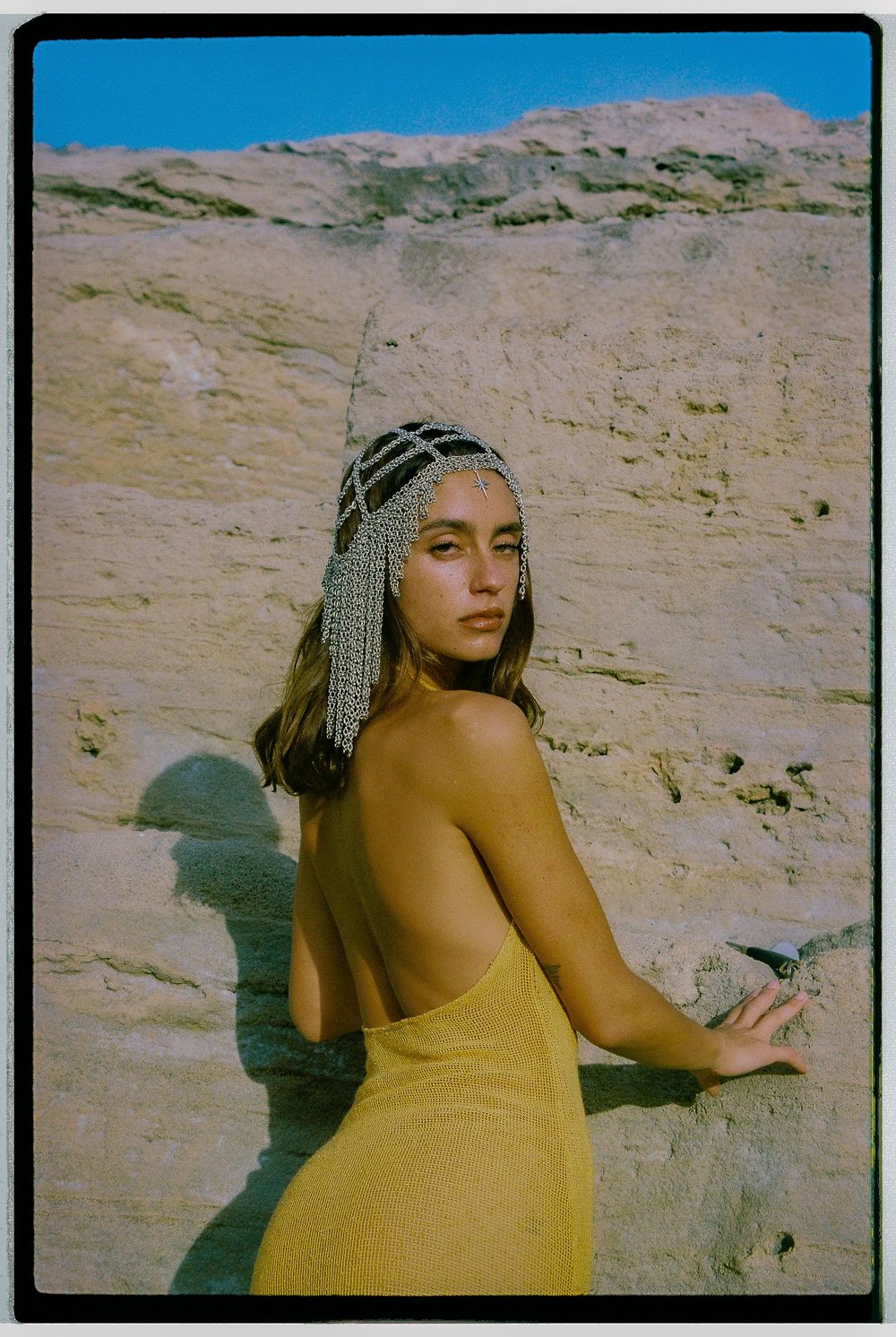 Figure in a yellow dress poses against desert rock formations in warm sunlight.