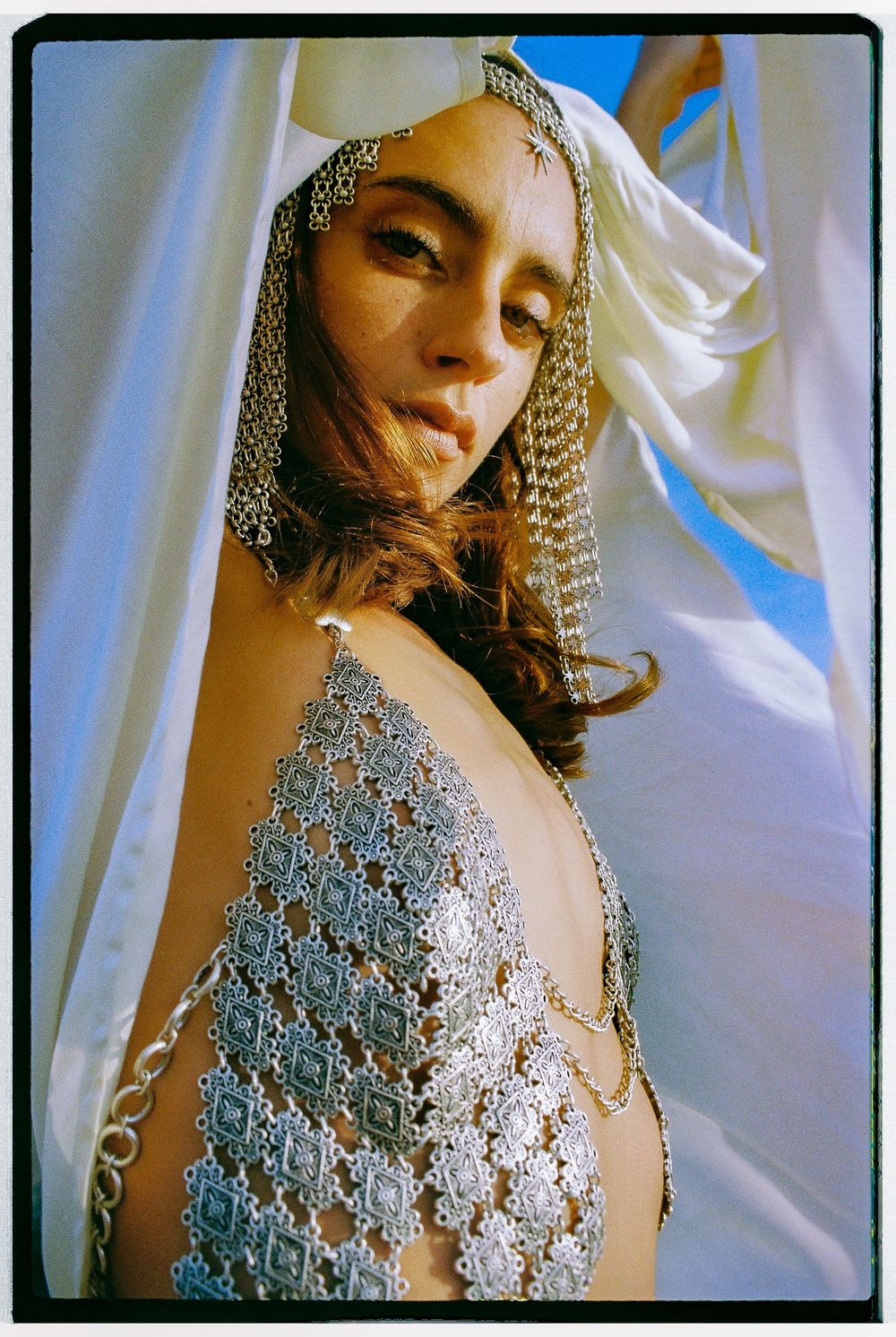 Artistic fashion portrait featuring an intricate silver beaded mesh top against a white draped fabric backdrop.