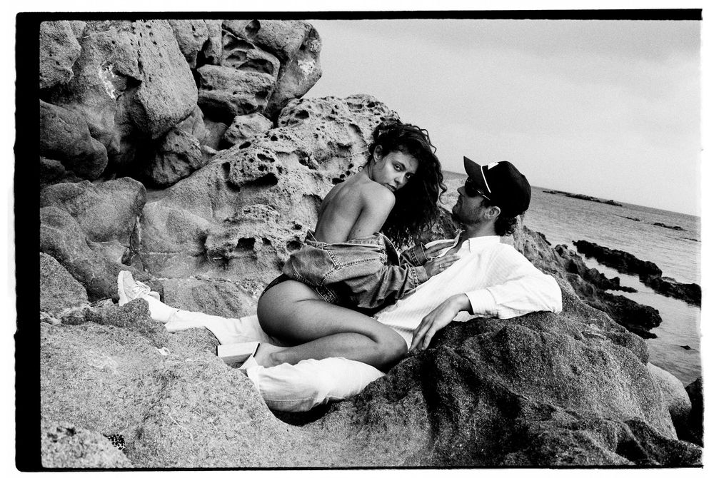 Black and white photographs of people relaxing on a sandy beach with rocks visible in the background.