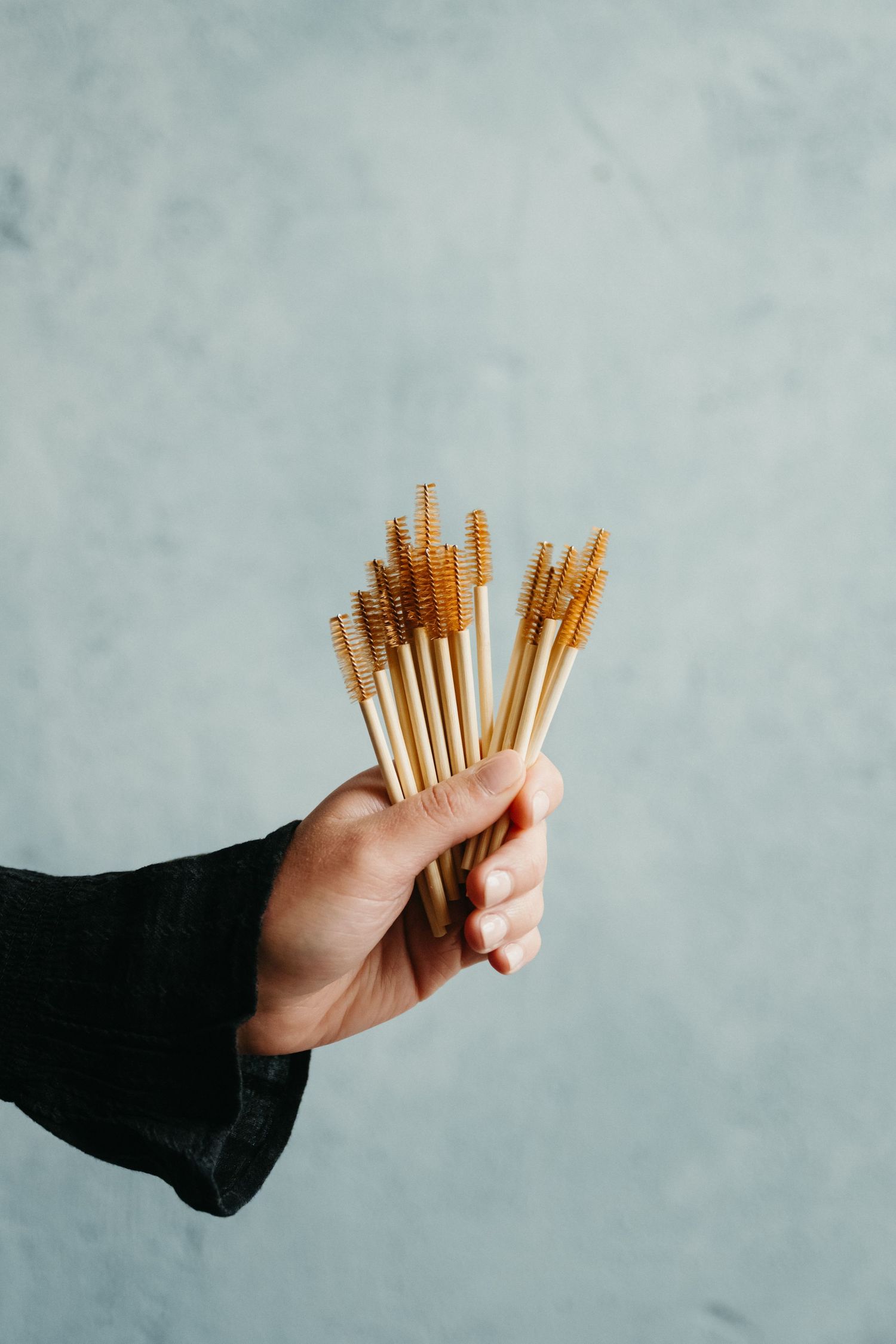 A hand holds a bundle of golden breadsticks against a gray background in a minimalist composition.