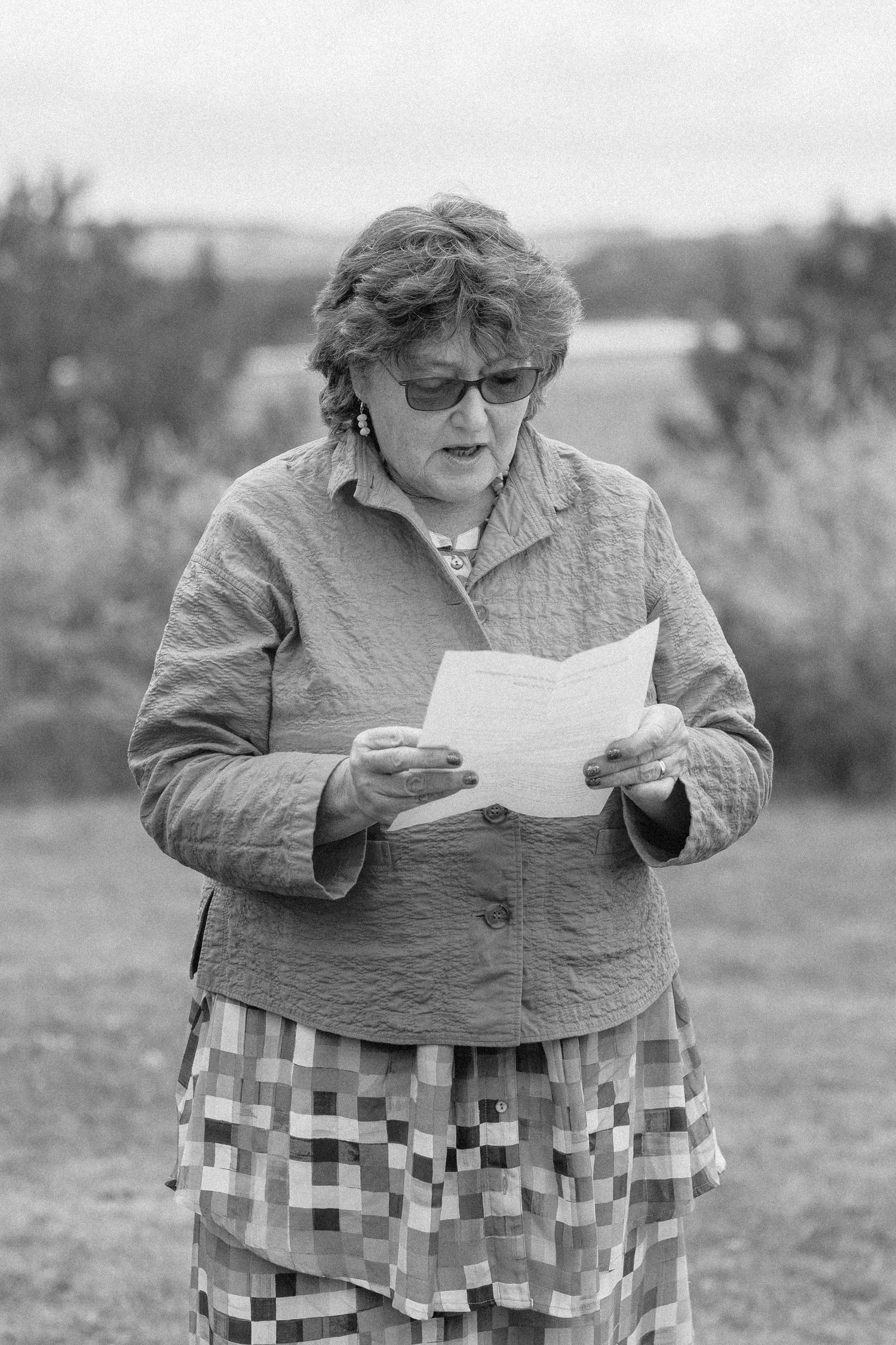 A person in a patterned skirt and jacket sits outdoors reading papers in a series of black and white photographs.