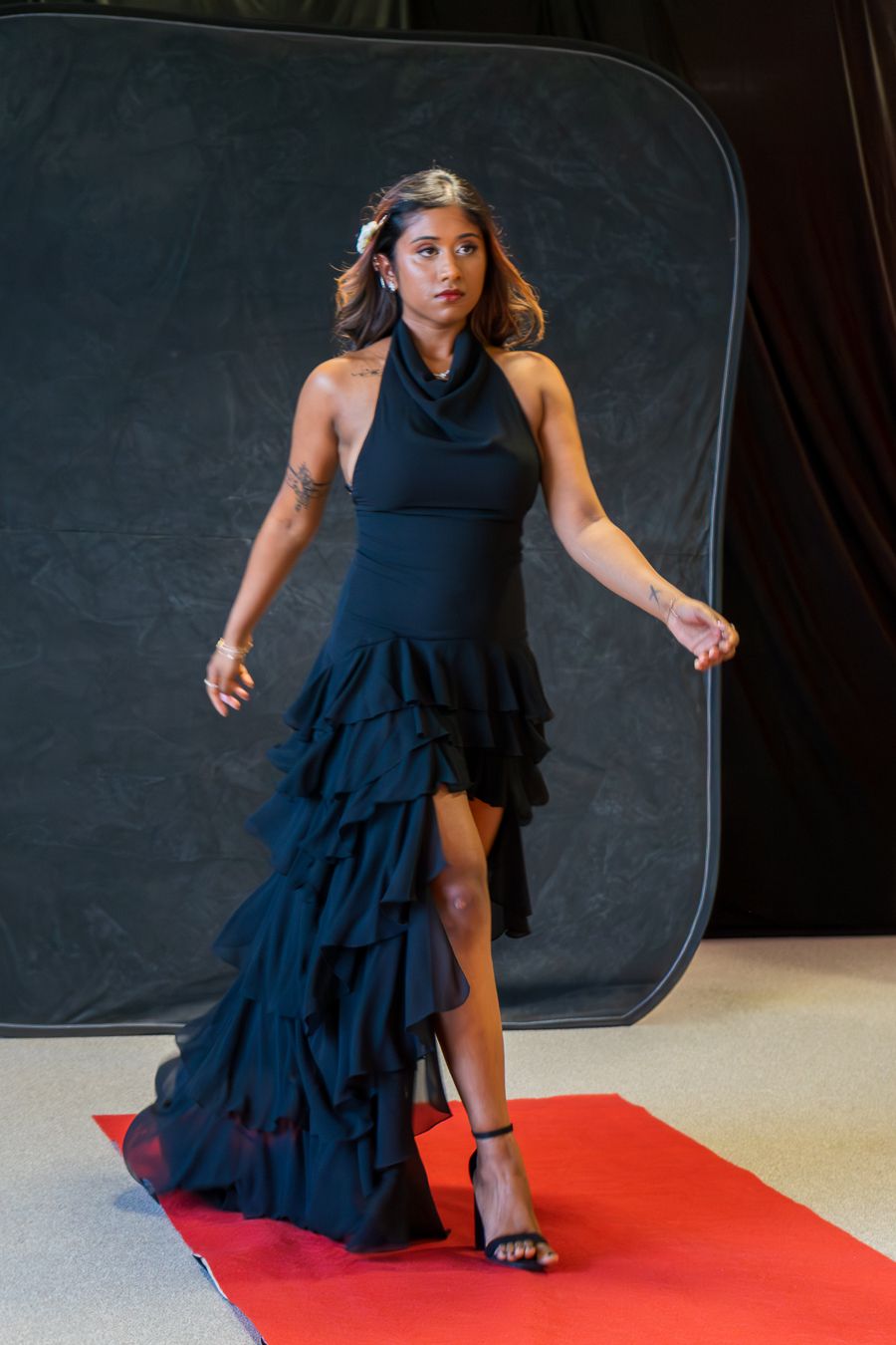 Dancer in a navy blue ruffled dress performs an expressive movement sequence on a red floor mat.