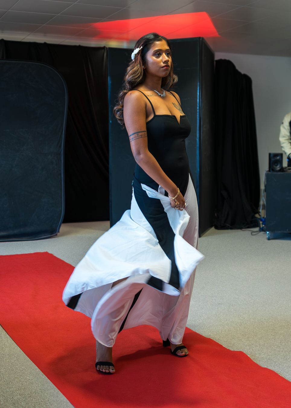 A person in black top and white pants performs a dance sequence on a red carpet in what appears to be a studio space.