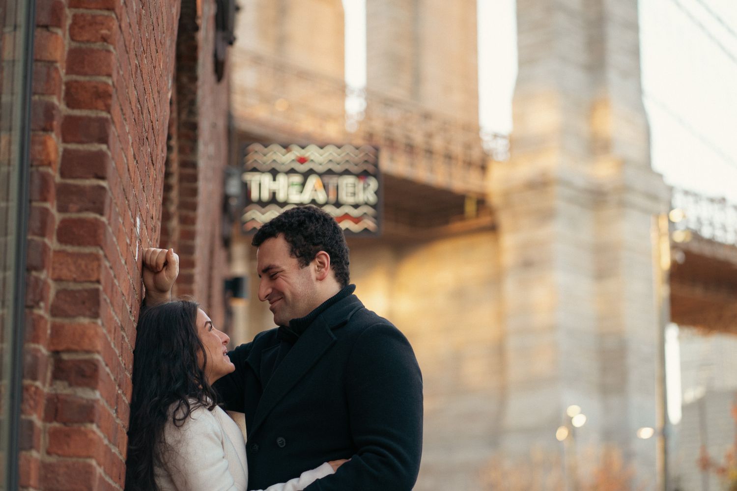 A couple shares a romantic moment on a city street with brick buildings and window reflections in black and white.