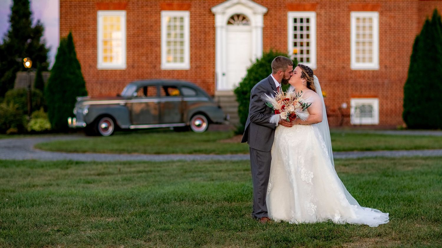 frederick maryland wedding photographer A tender moment between newlyweds outside a classic brick building with vintage car in background.