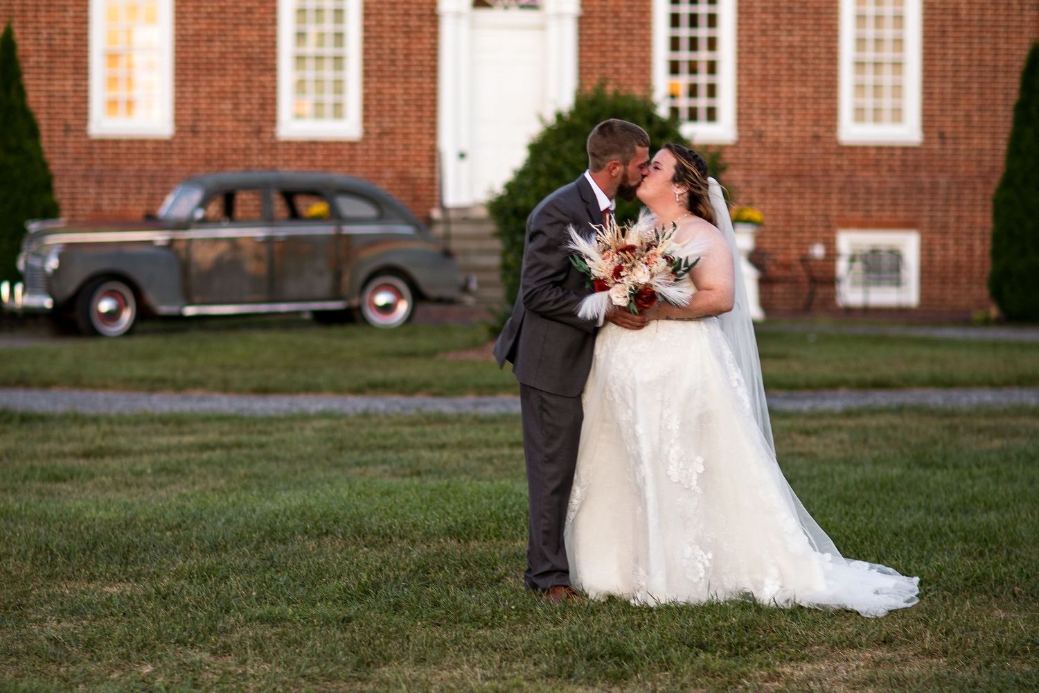 frederick maryland wedding photographer Newlyweds share an intimate moment outside a historic brick building with vintage automobile.
