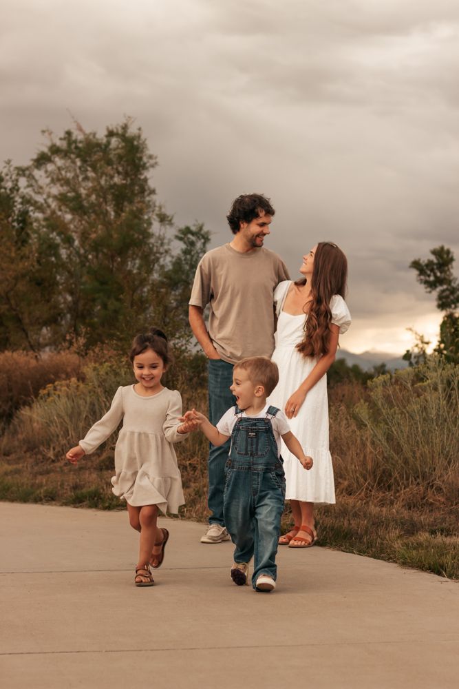 A family walks together on a concrete path at sunset through a natural outdoor setting. |Westminster Colorado Family Photographer