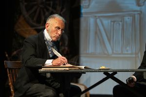 theatre photography Brighton. actor sits on stage writing with a feather quill in victorian costume in theatre show great expectations.
