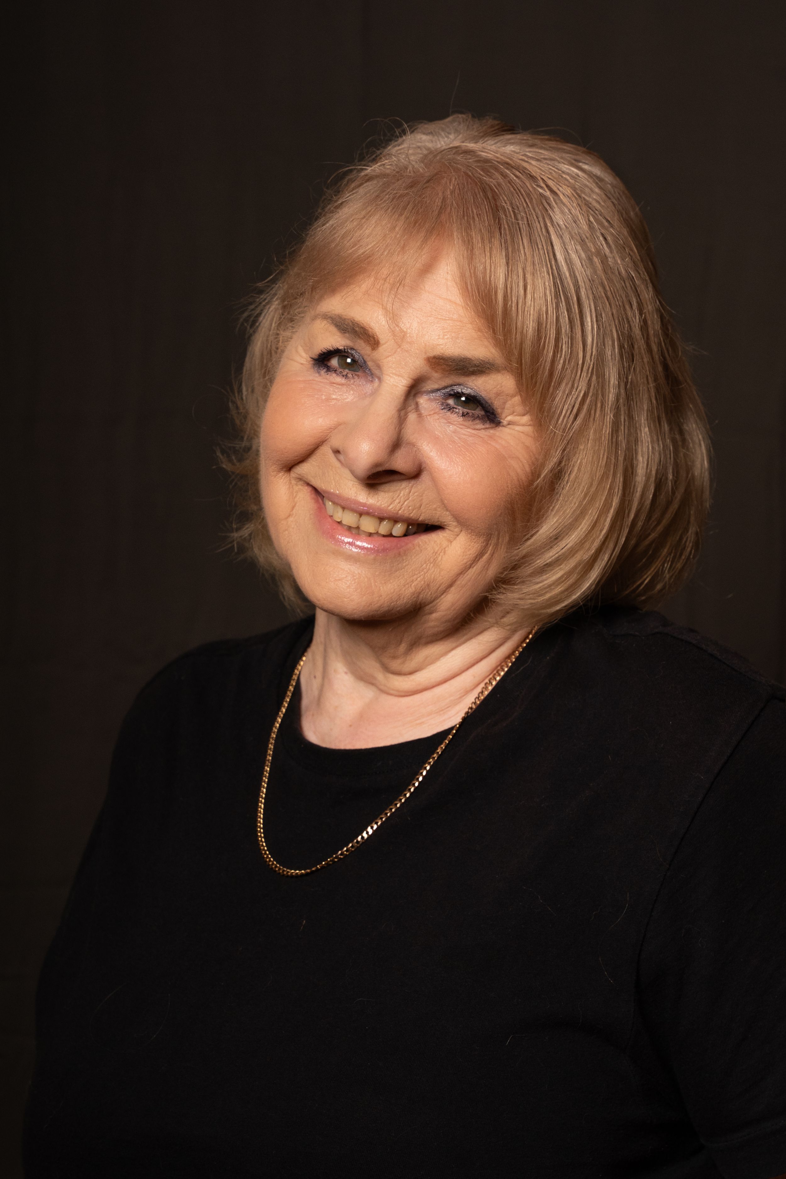 head shot photography Brighton. and actress with short blond hair smiles at the camera with a dark backdrop in a headshot photo