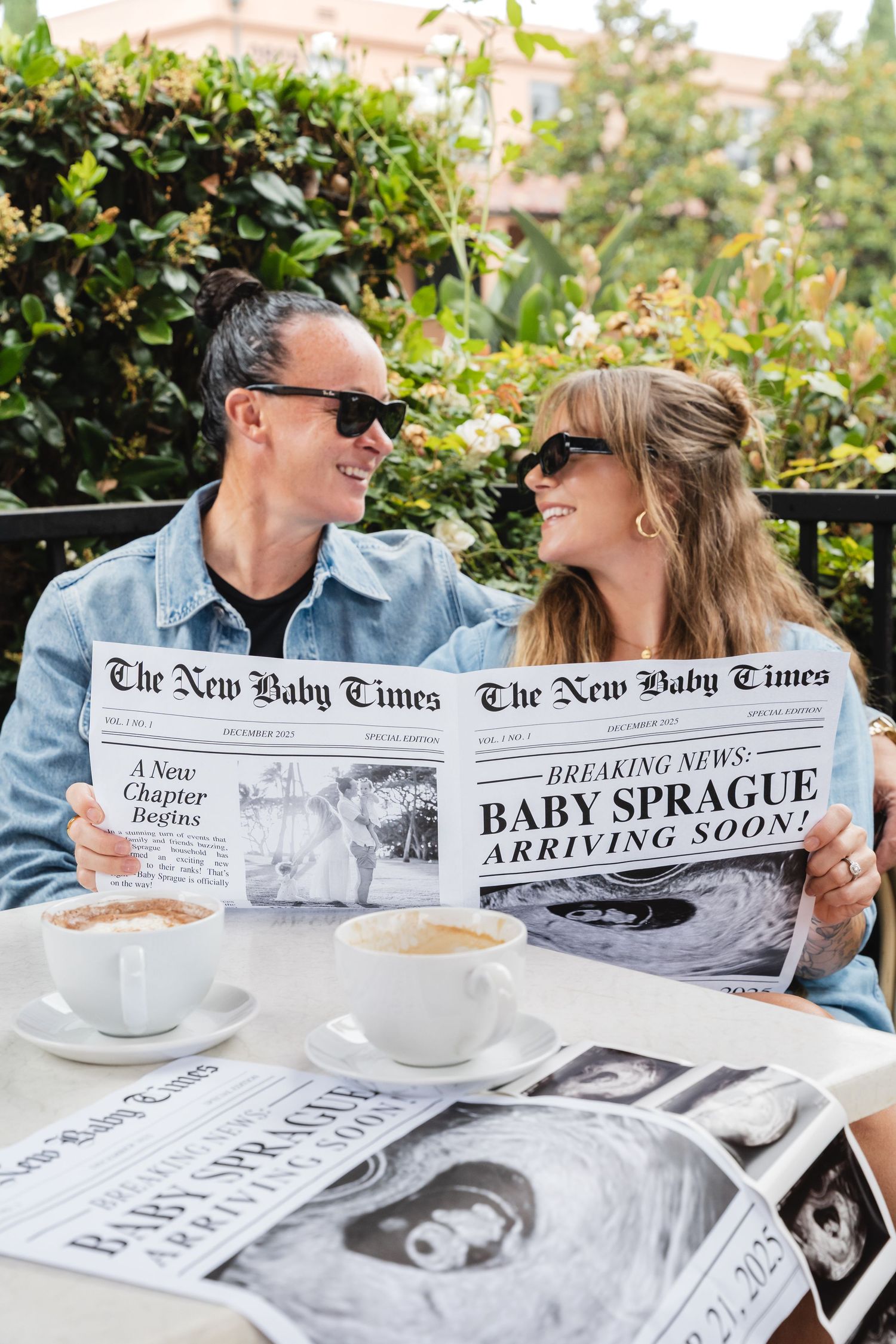 Couple holding baby announcement newspaper during maternity session at coffee shop while wearing glasses