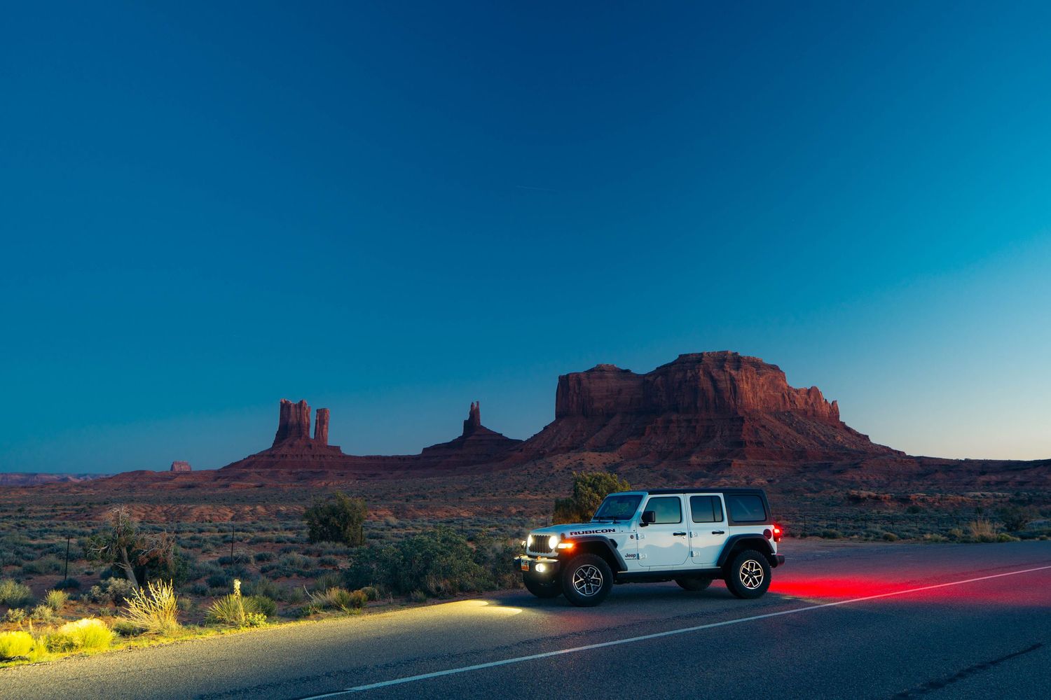 Light trails from passing cars illuminate the winding desert road through Monument Valley at dusk.
