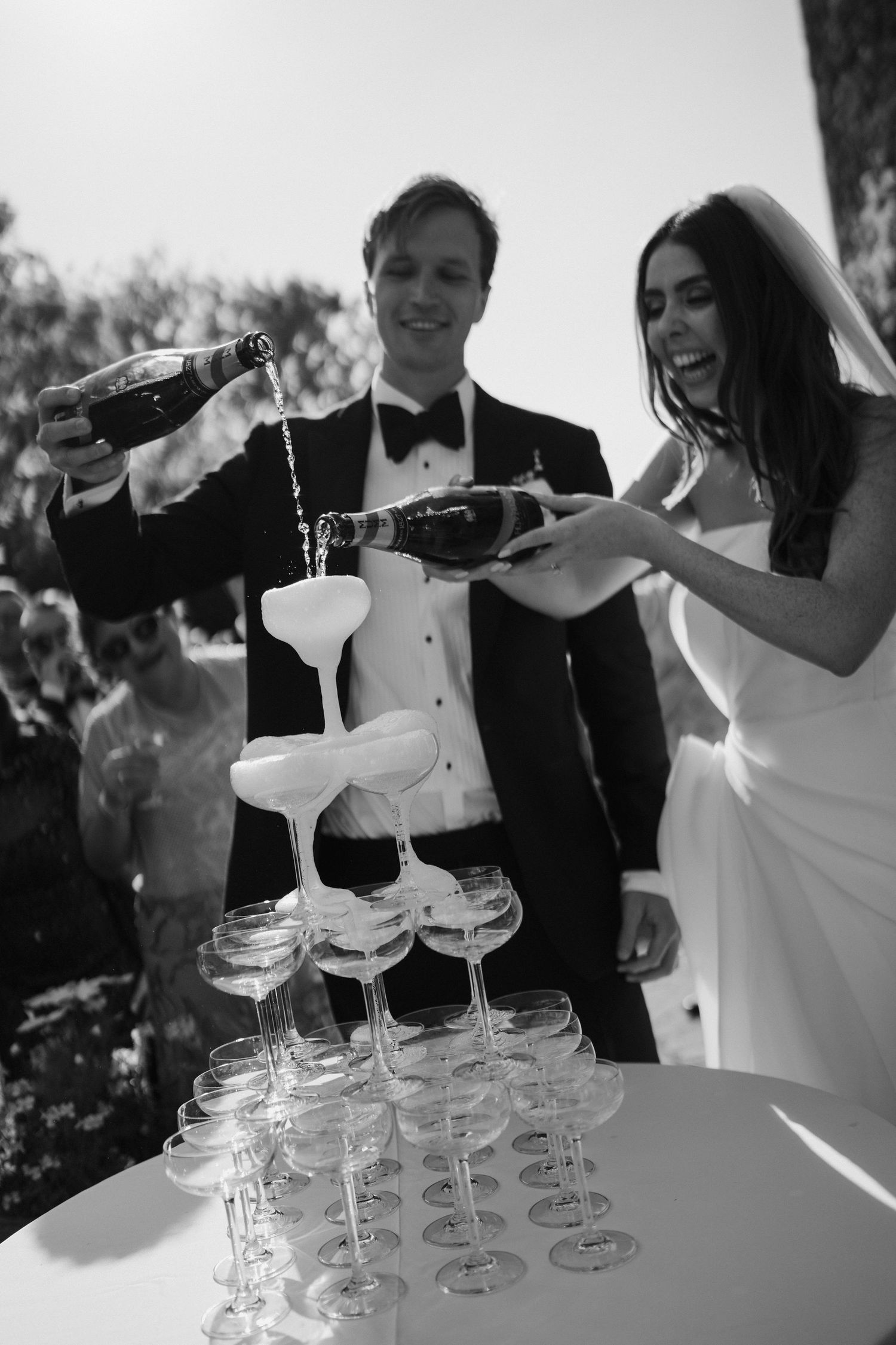 bride and groom pouring champagne into a tower of champagne glasses while their guests surround them cheering at dewsall court in hereford