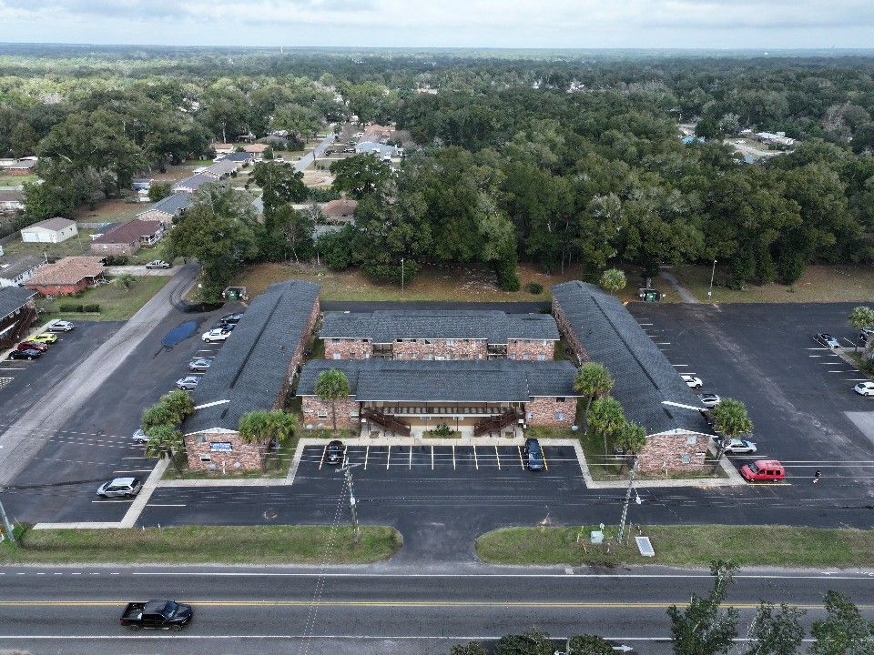 Aerial view of a commercial strip mall with parking lot and surrounding landscape.