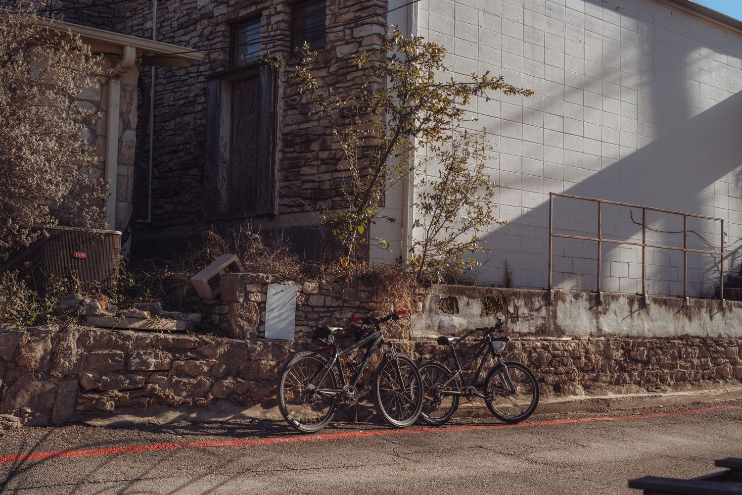 Vintage bicycles lined up against a rustic stone wall with sunlight casting dramatic shadows on the ground.