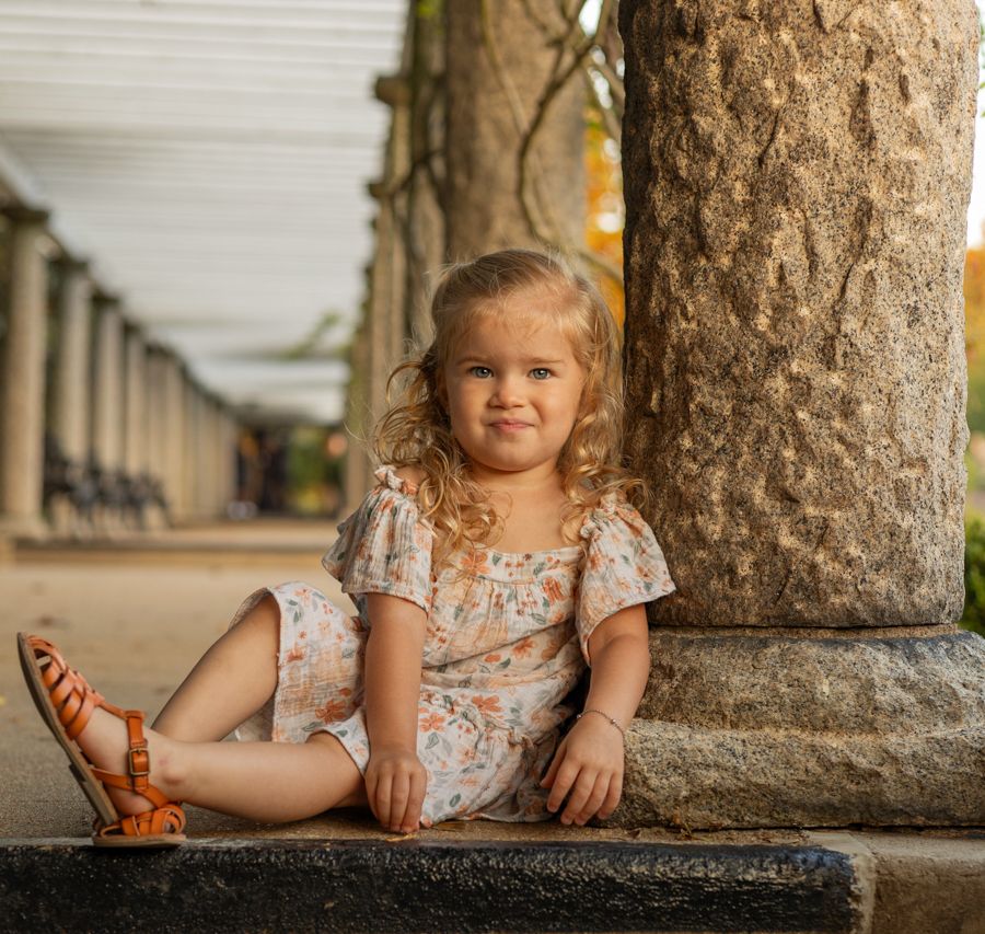 toddler girl making a fun face leaning against. column