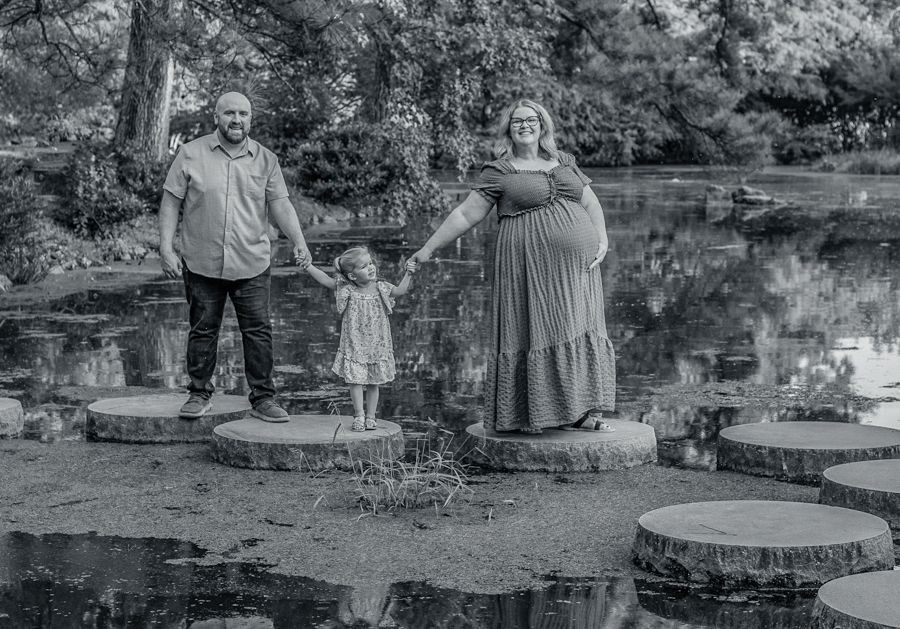 black and white image of a Maternity session with mom, dad, and daughter. Walking on stone path in Japanese garden. RVA