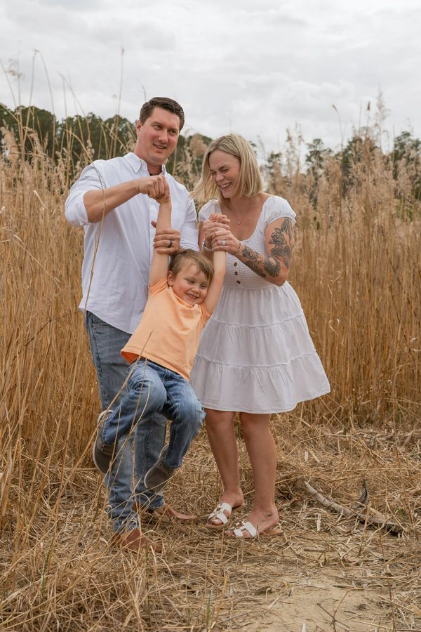 mom and dad holding son and swinging him, laughing located in gloucester virginina