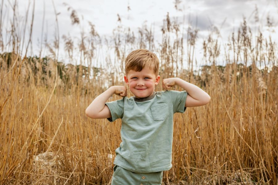 A young child plays and poses in a field of tall brown grass on a sunny autumn day.