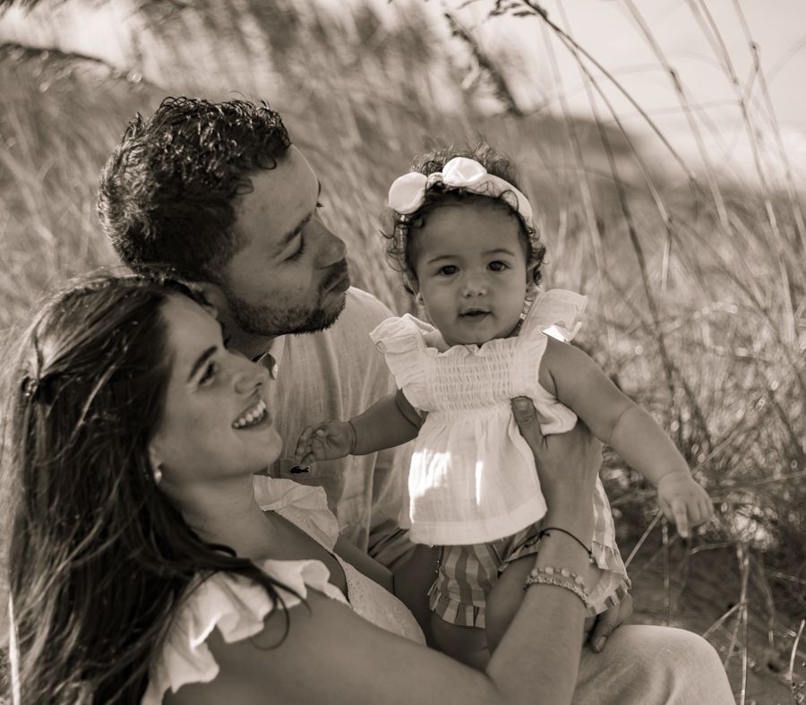 black and white image of mom and dad holding and smiling at daughter in the beach grass