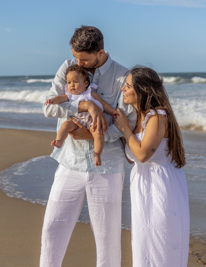 mom and dad holding daughter on virginia beach oceanfront kissing her and laughing