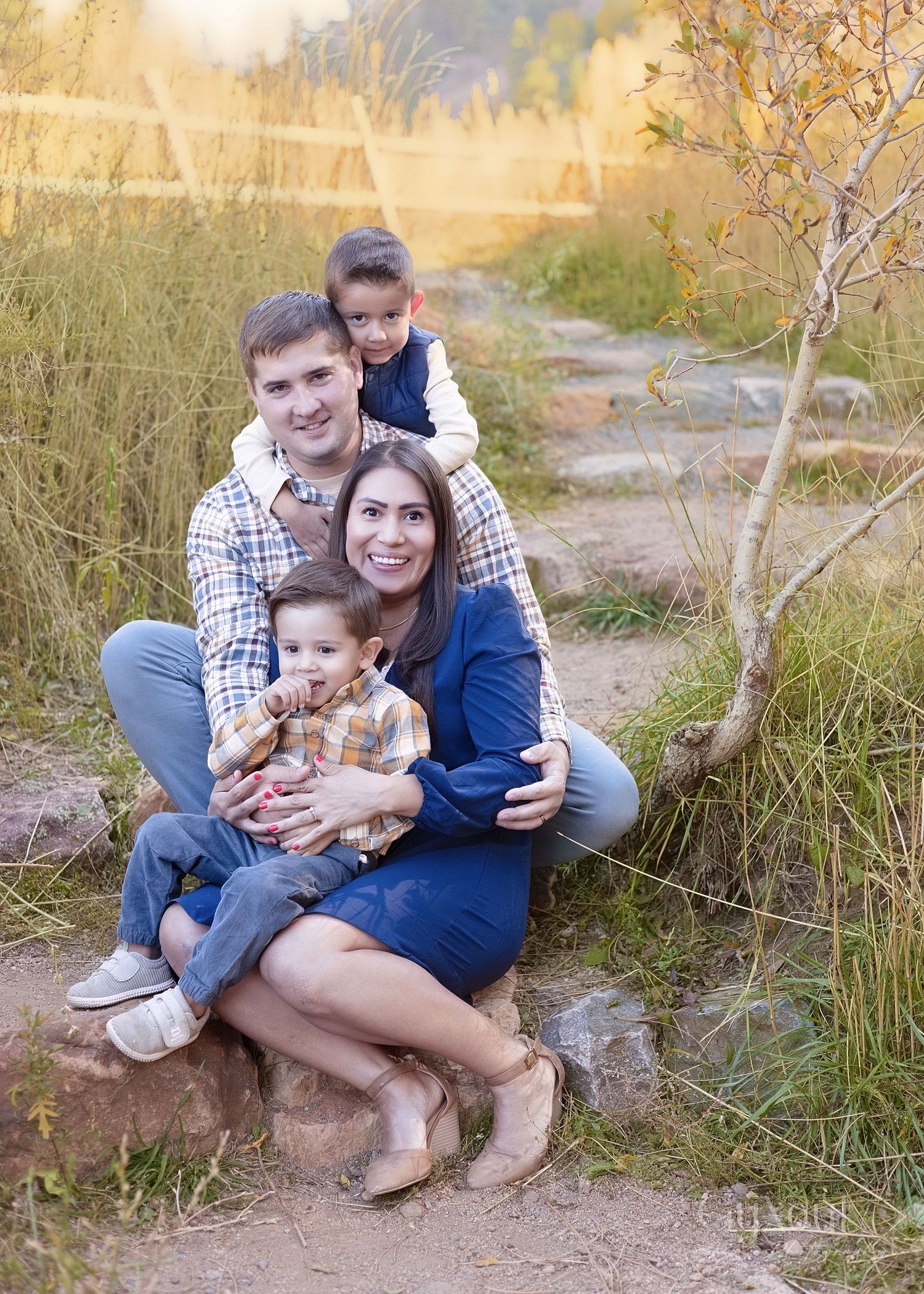 Family sitting together on a rocky path surrounded by autumn grass during an outdoor photoshoot at golden hour.
