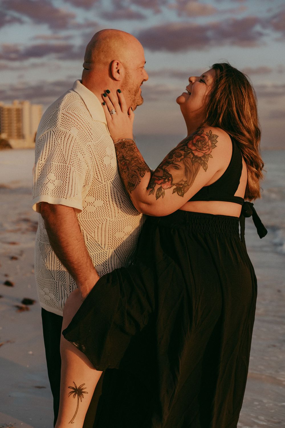 Romantic couple embraces on beach at sunset with dramatic cloudy sky in background.