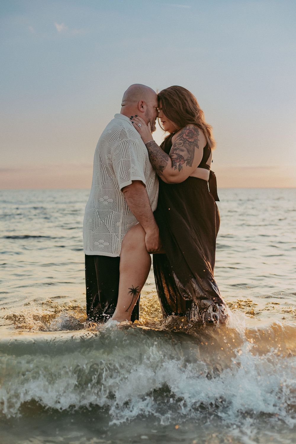 Couple plays in ocean waves during golden hour photoshoot at the beach.