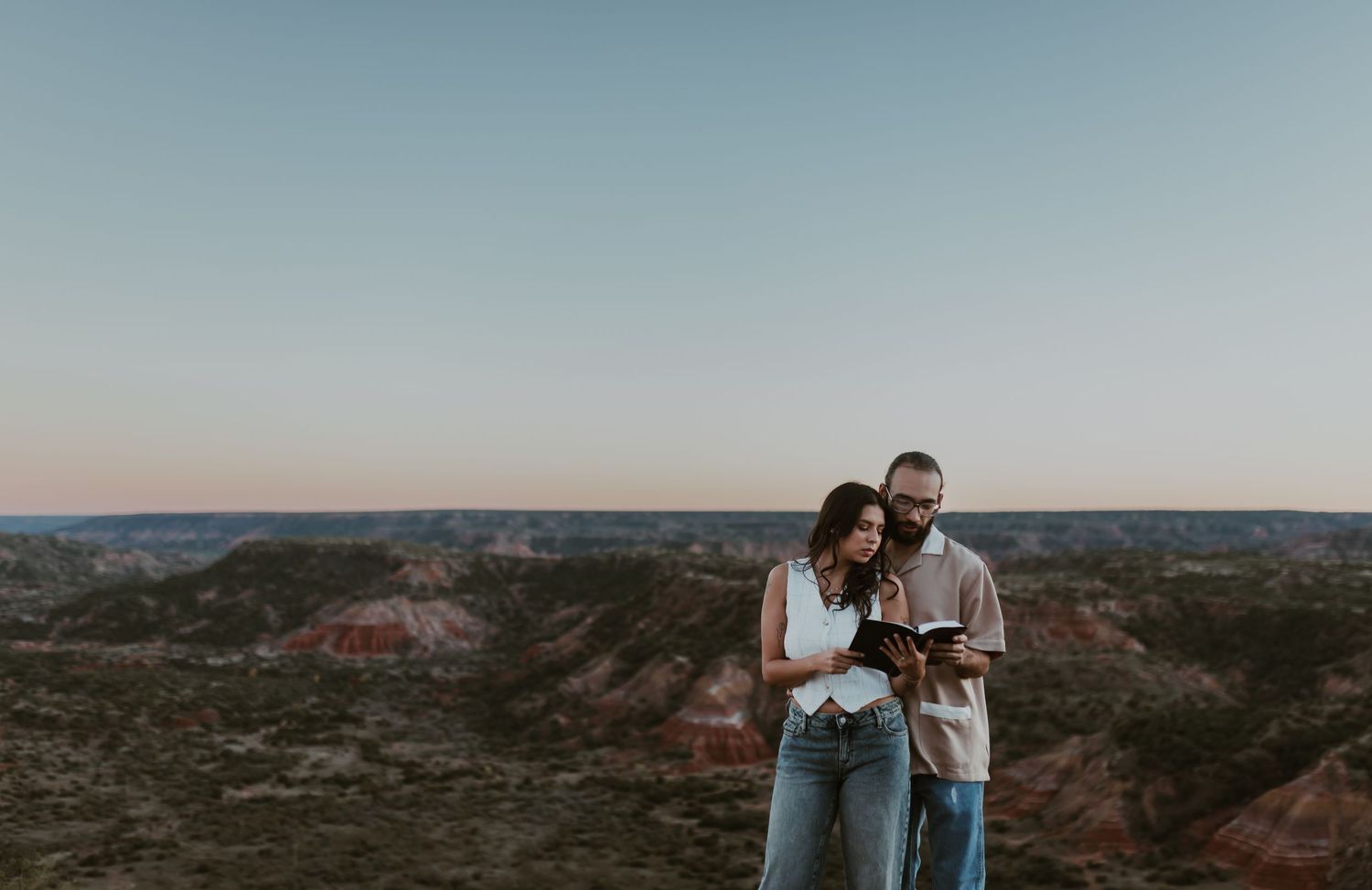 Couple reading a book together at sunset overlooking a scenic red rock canyon landscape.