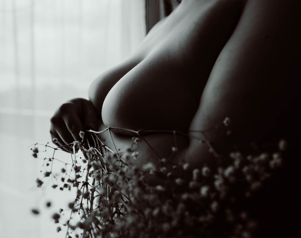 Black and white artistic boudoir photograph of a woman with delicate baby's breath flowers in soft natural lighting.