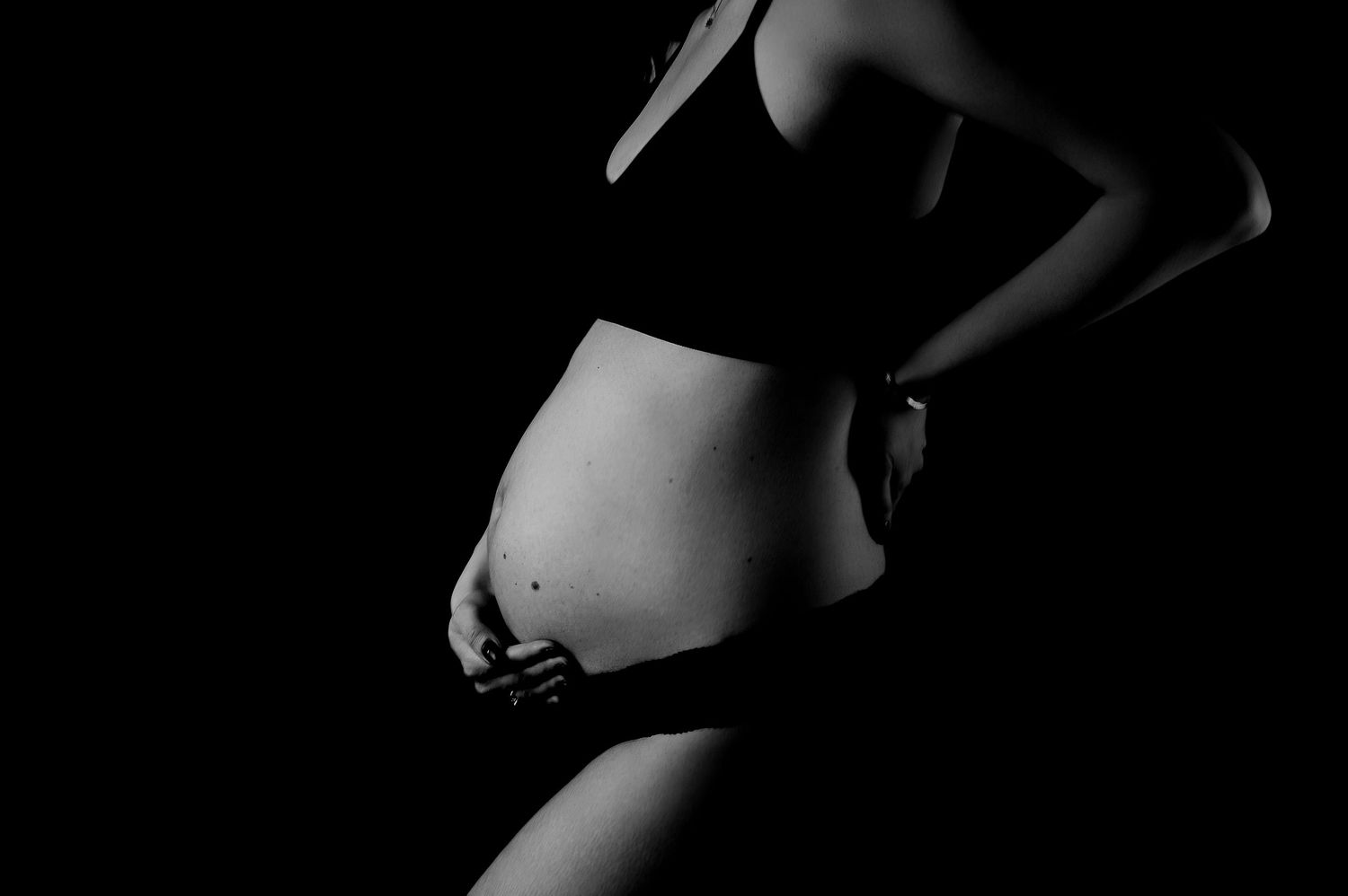 A black and white artistic nude photograph showing the curves and shadows of a person's back in dramatic lighting.