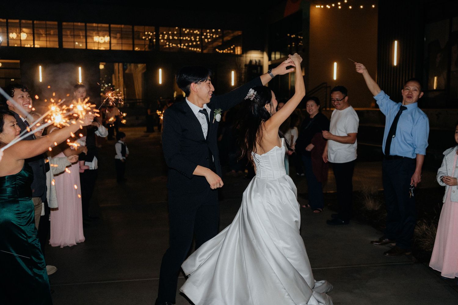 Wedding guests dancing and celebrating on a dark dance floor with string lights overhead.