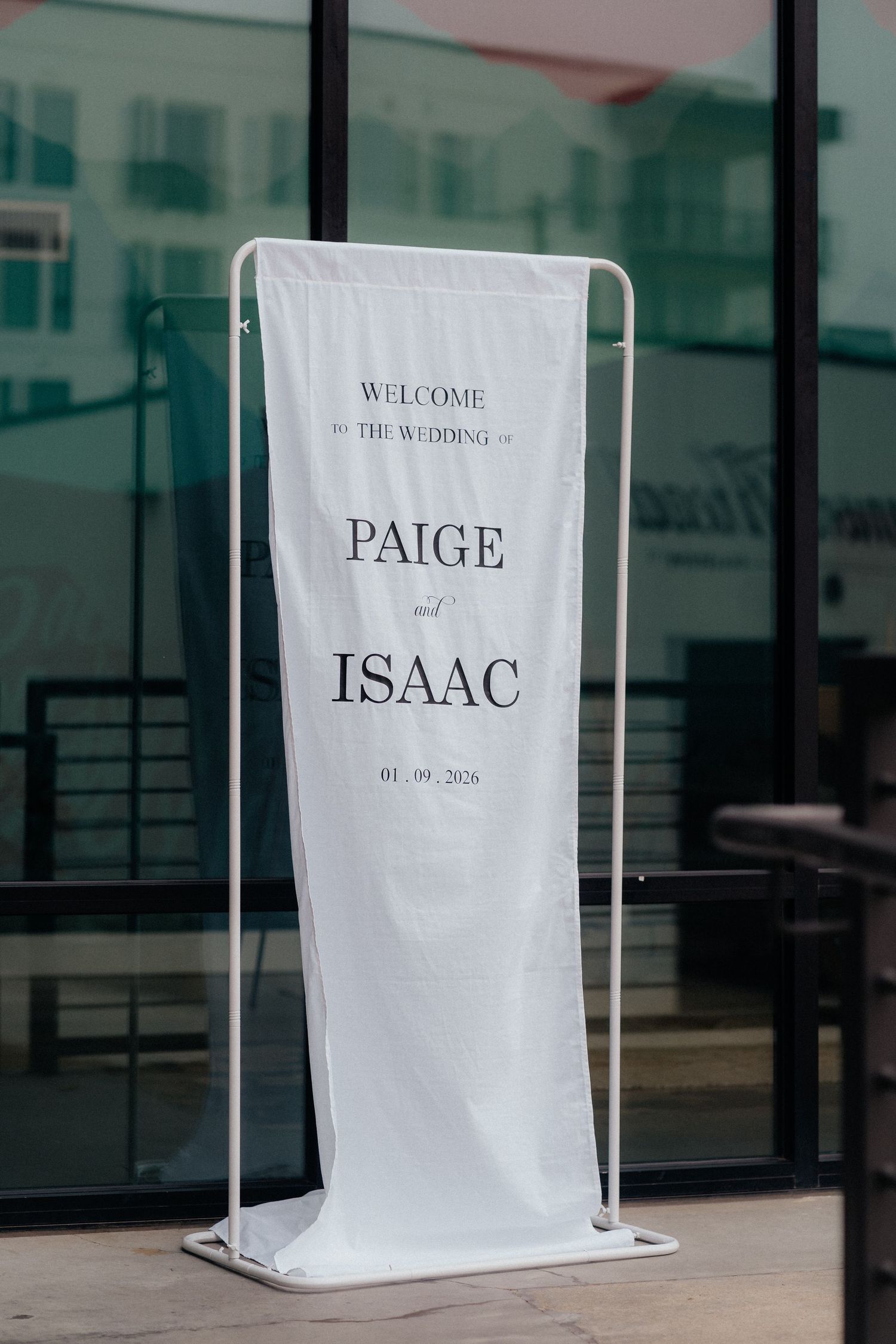 White welcome signs for a wedding displayed against glass windows with modern typography.
