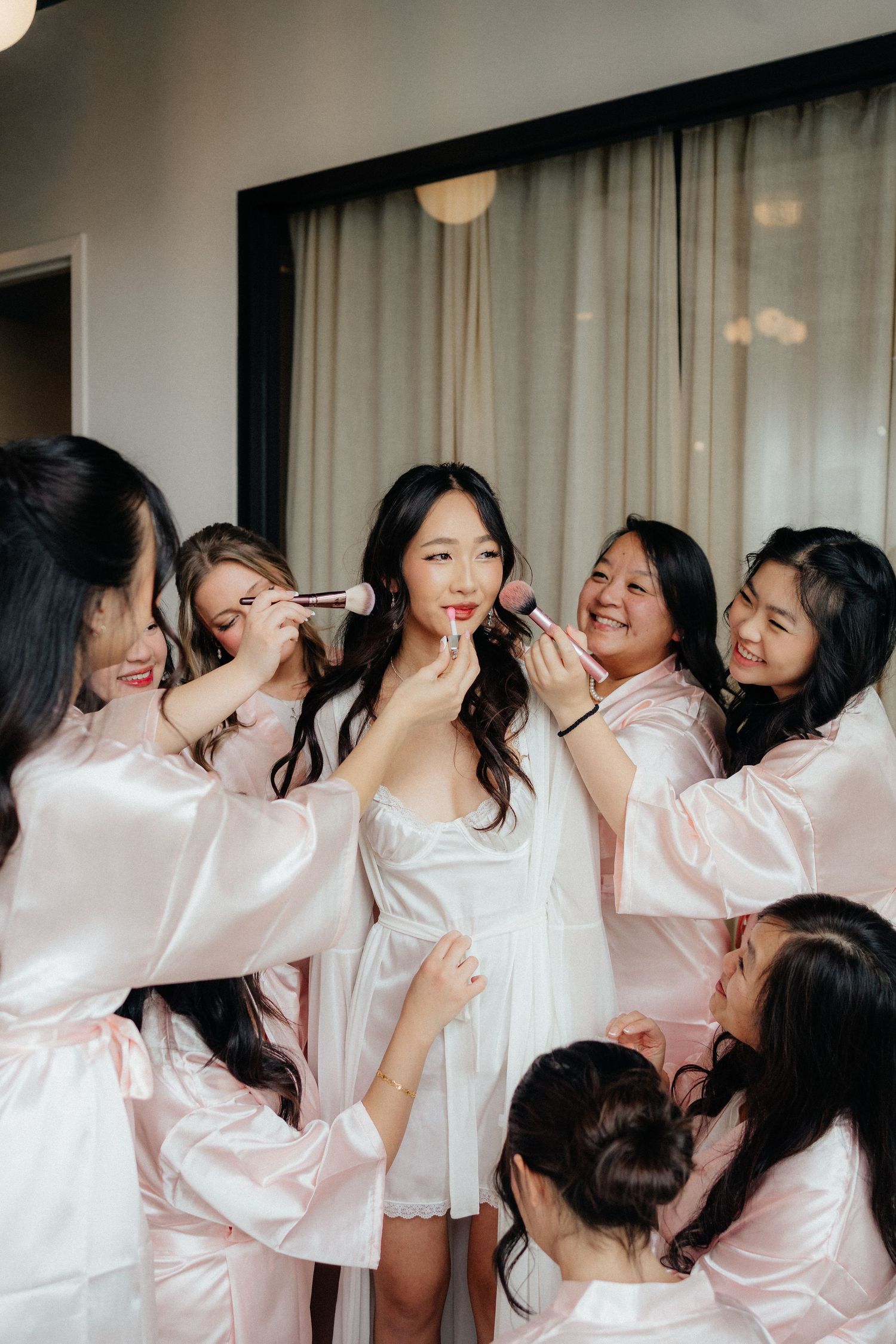 A group in matching pink satin robes share laughter and joy during a pre-wedding getting ready moment.