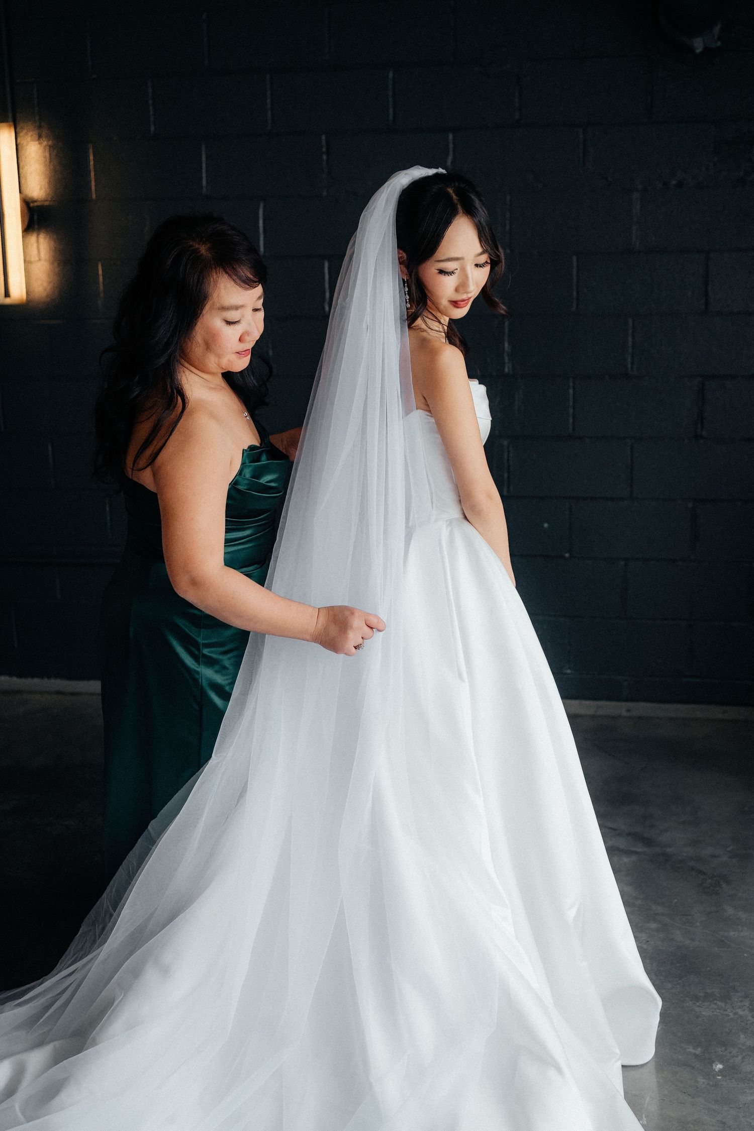 Elegant bridal fashion moment captured in a dark moody setting with flowing white gown and veil creating movement.