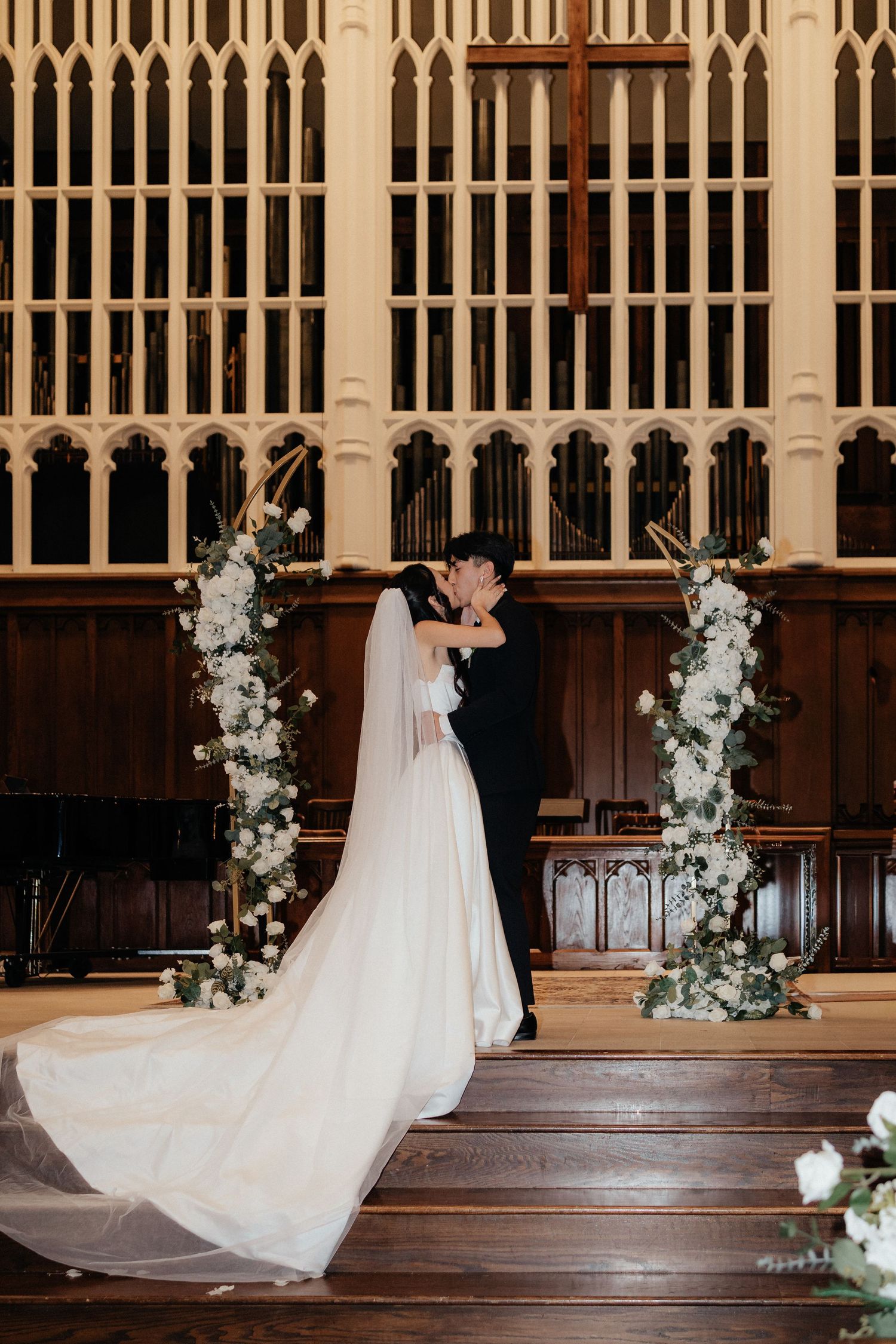 Wedding ceremony setup in elegant church with wooden paneling and white floral arch decorations.