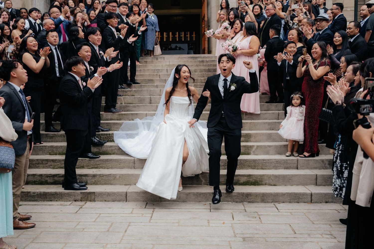 Large group of wedding guests gathered on stone steps for a celebratory outdoor photo.
