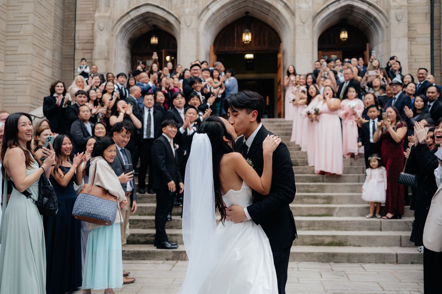 Wedding ceremony guests gathered on stone church steps watching the newlyweds.