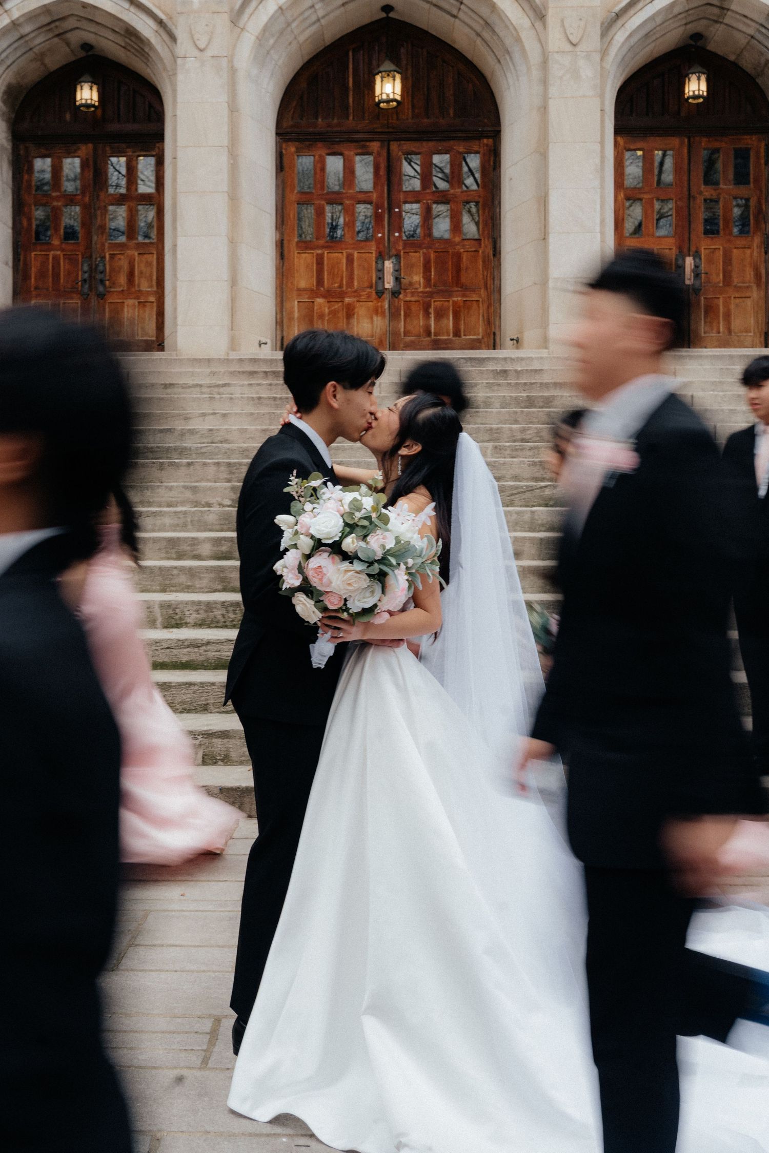 Wedding party in motion blur outside historic stone building with arched doorways and warm lighting.