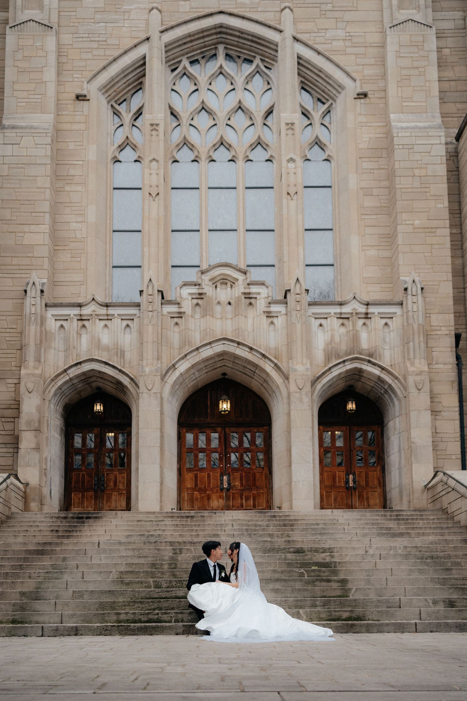 Gothic church facade with ornate stone archways and wooden doors provides elegant backdrop for wedding photos.