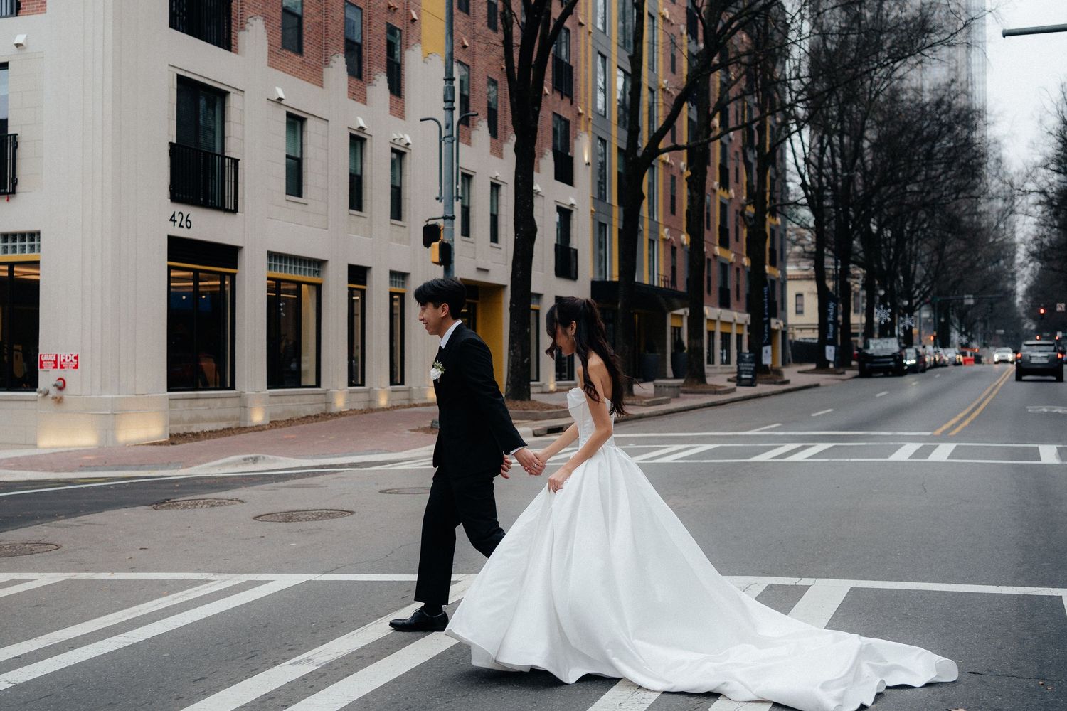 Newlyweds walking together on an urban street with historic brick buildings in the background.