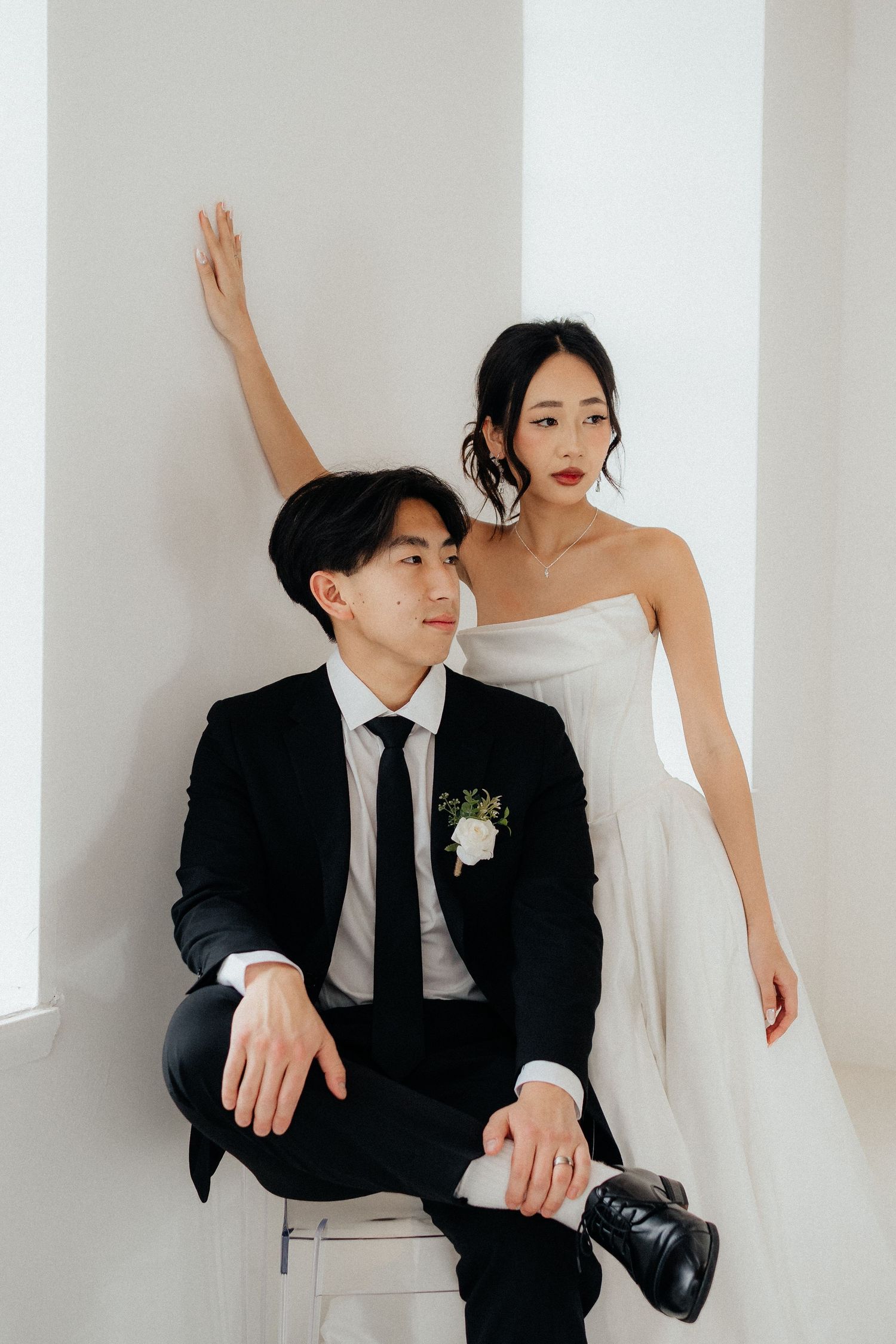 Elegant couple in black and white wedding attire pose artistically against minimalist white walls.