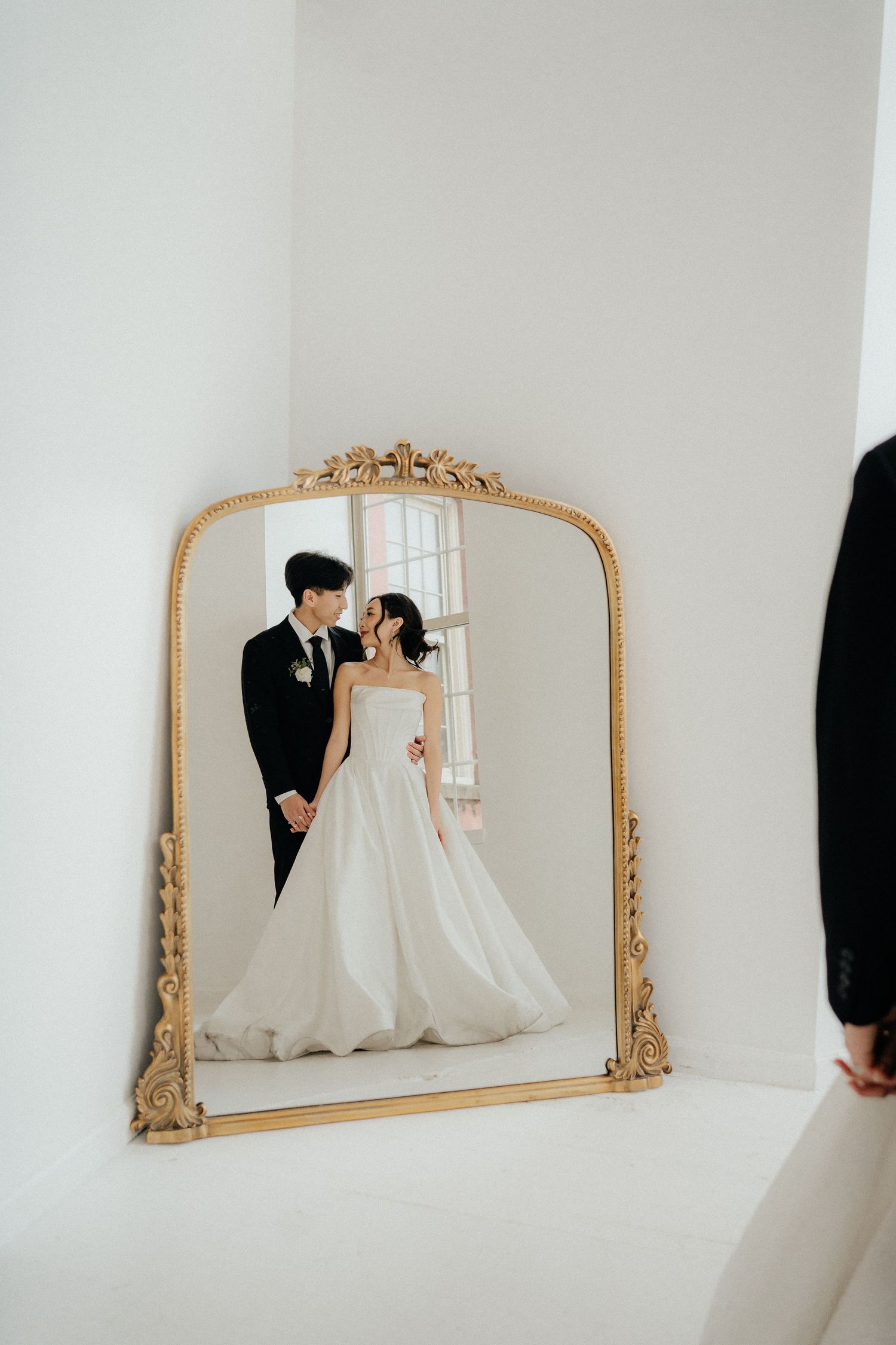 Ornate gold-framed mirrors on a white wall reflect formal attire and elegant decor.