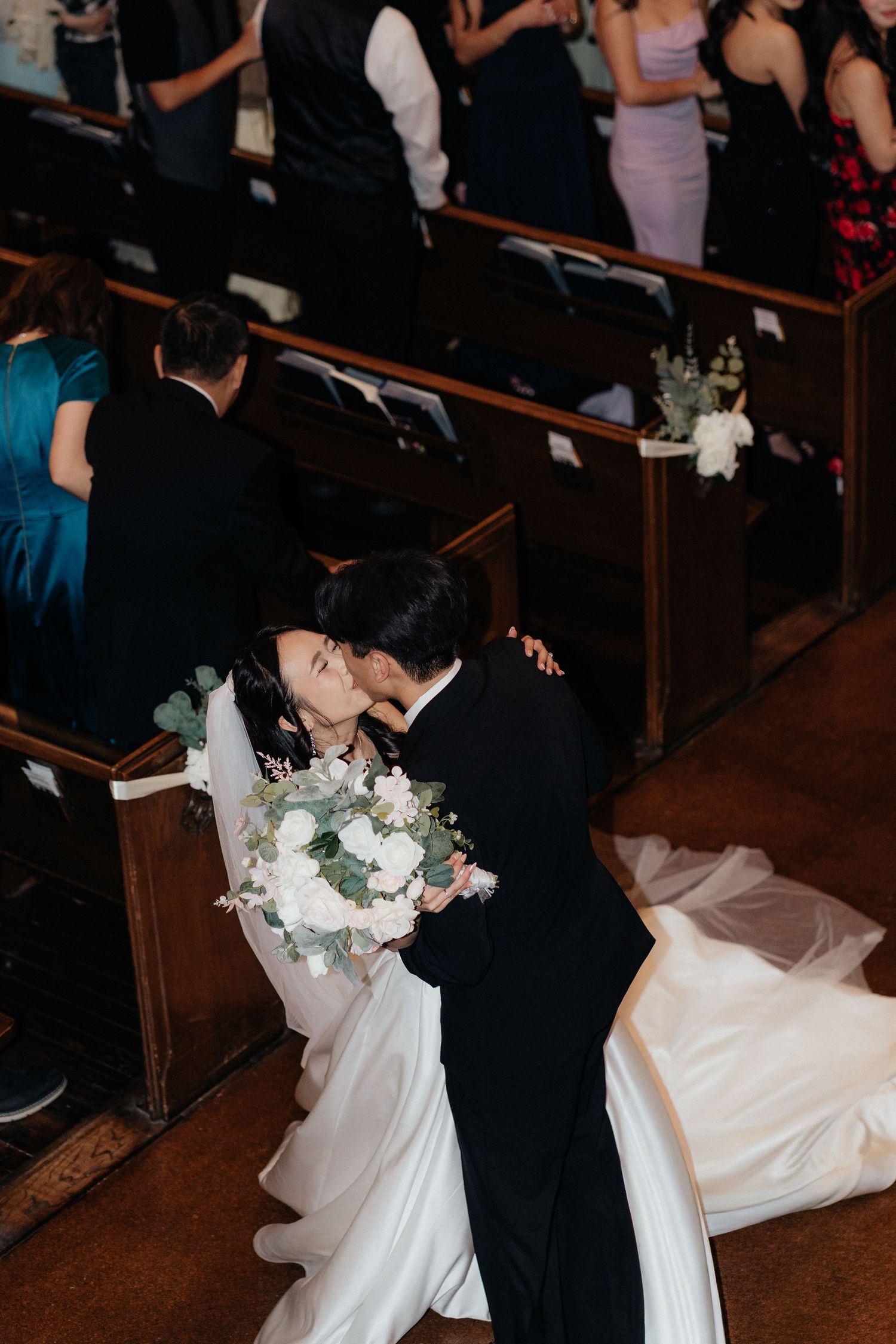 A romantic wedding moment captured as a couple shares their first kiss at the altar in a dimly lit church ceremony.