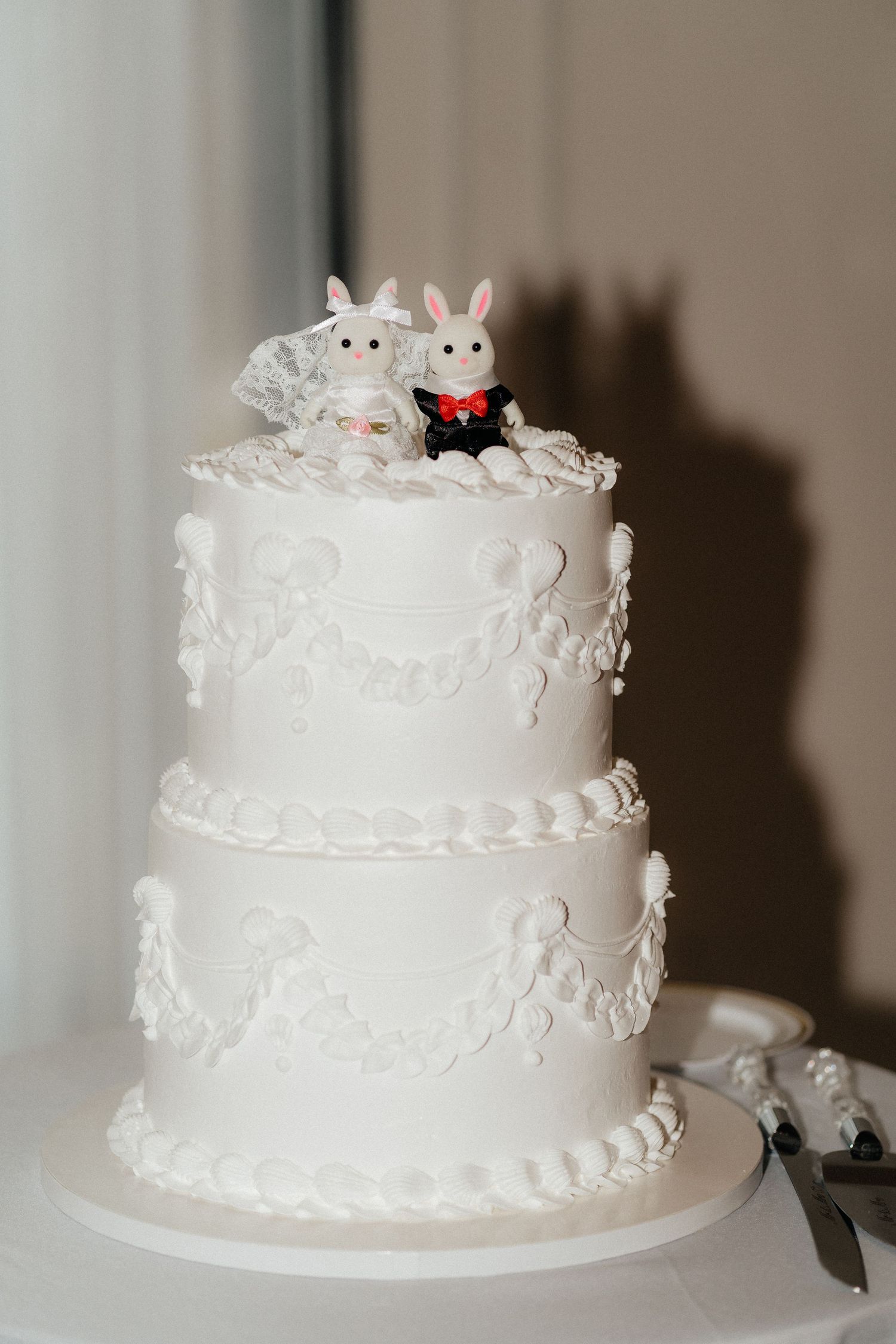 A white tiered wedding cake decorated with delicate frosting and topped with small bunny figurines.